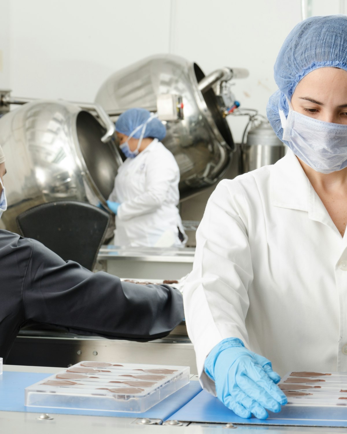 Food plant workers in PPE packing confectionery trays on a blue production belt