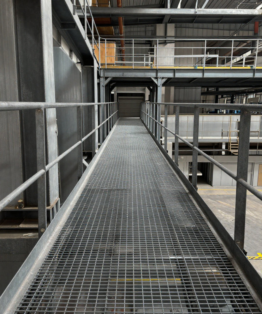 An industrial platform walkway with handrails spanning plant equipment