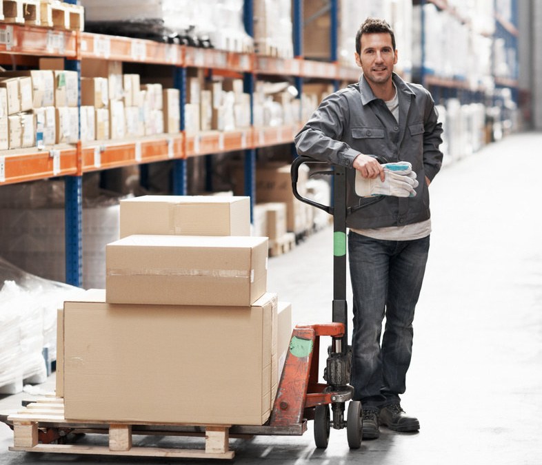 A warehouse operator with a hydraulic pallet trolley loaded with cartons